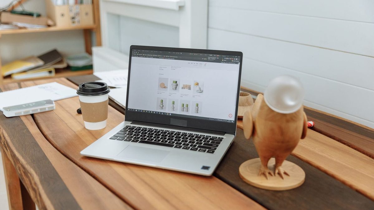 Un ordinateur portable posé sur une table en bois affiche la page d'accueil épurée d'un site vitrine, à côté d'un café et d'une figurine en bois.
