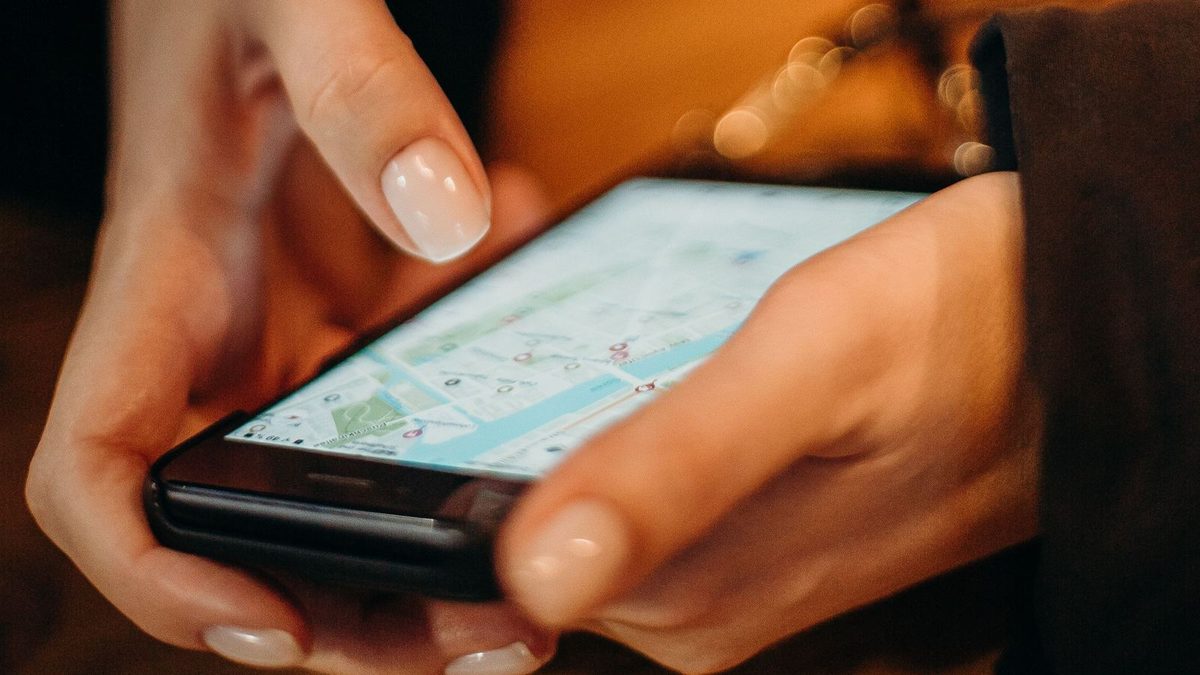 Deux mains tiennent un smartphone qui affiche le plan d'un quartier parsemé d'épingles de localisation.